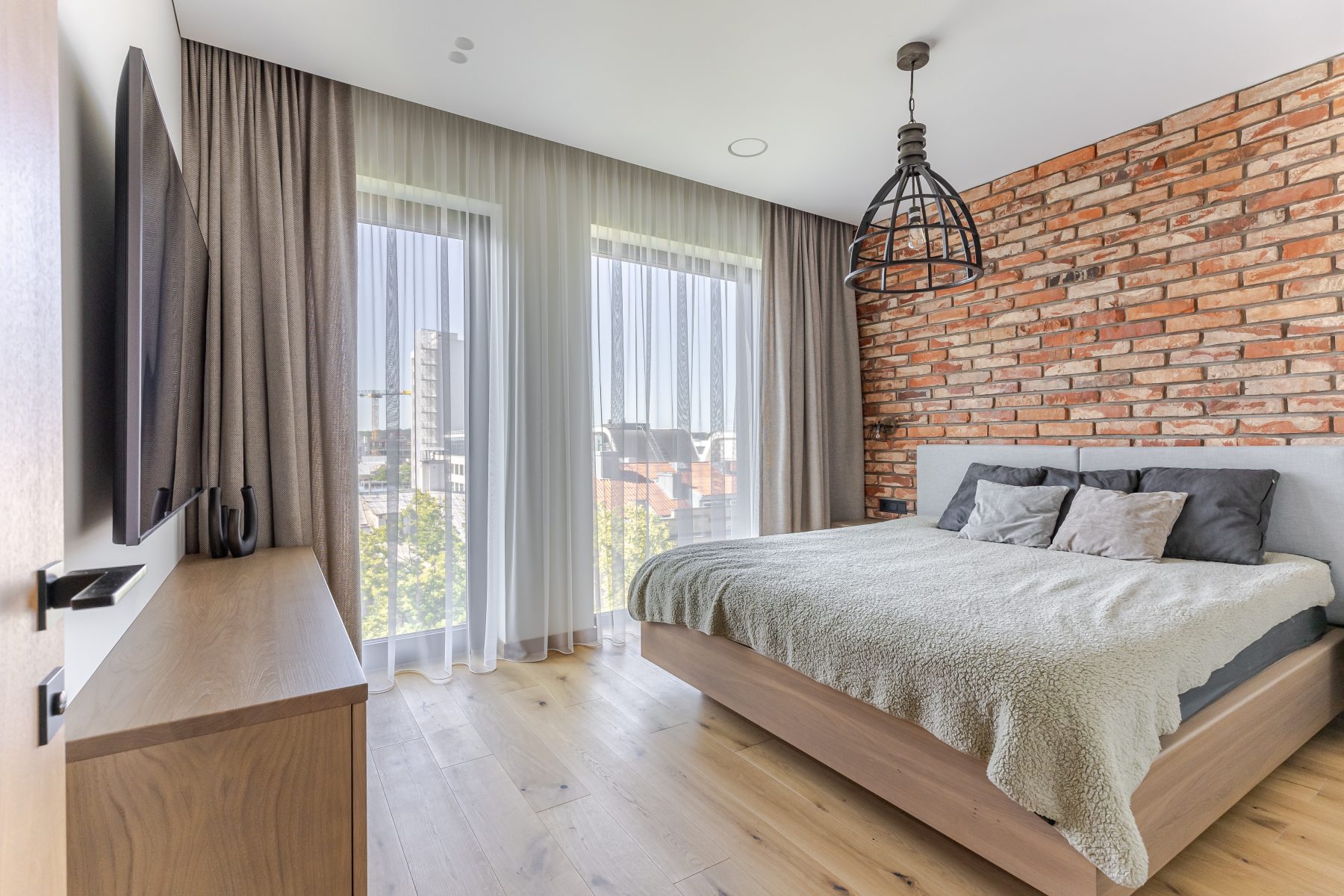 Miegamasis su natūralių plytų siena ir dideliais langais