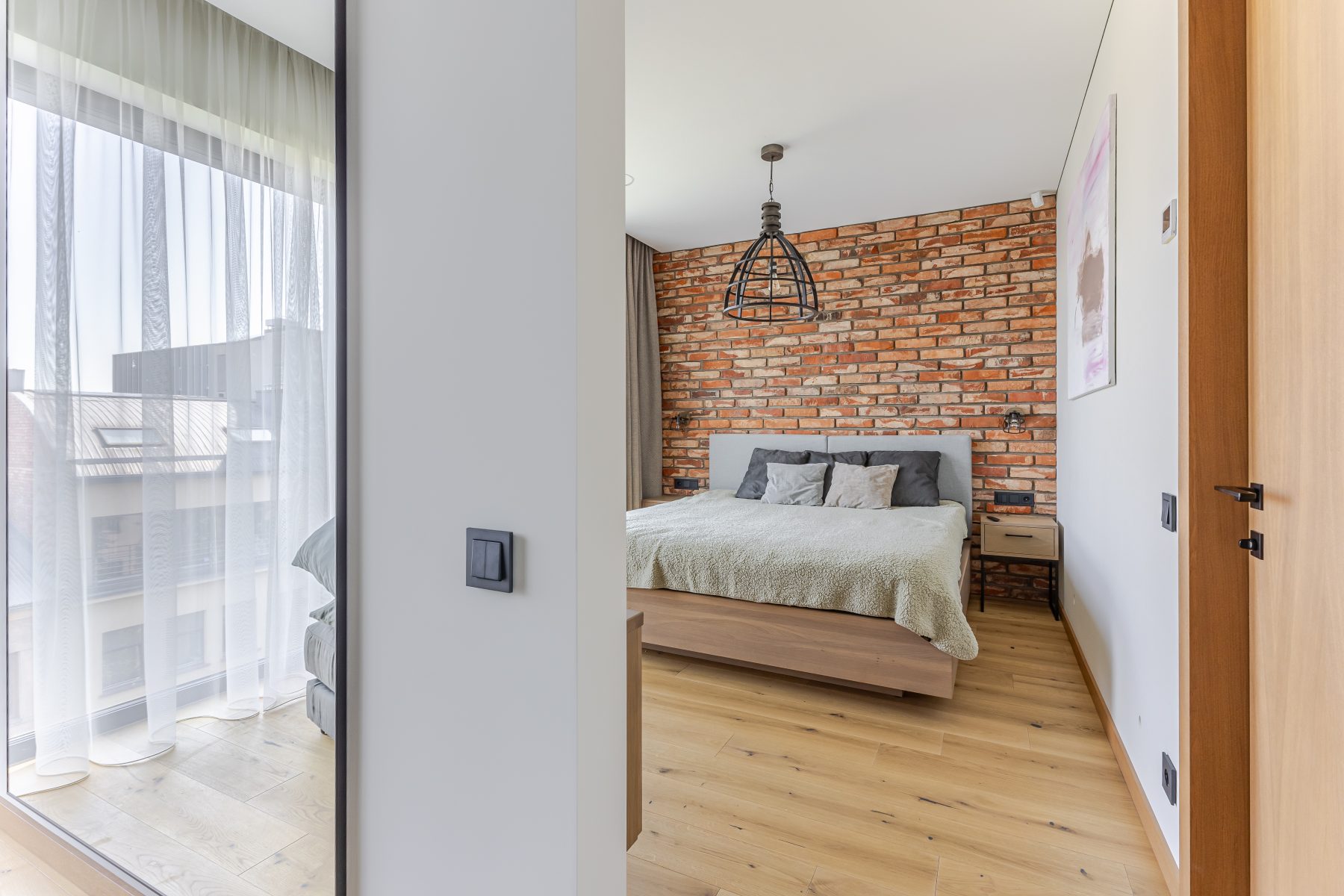 Miegamasis su natūralių plytų siena ir dideliais langais