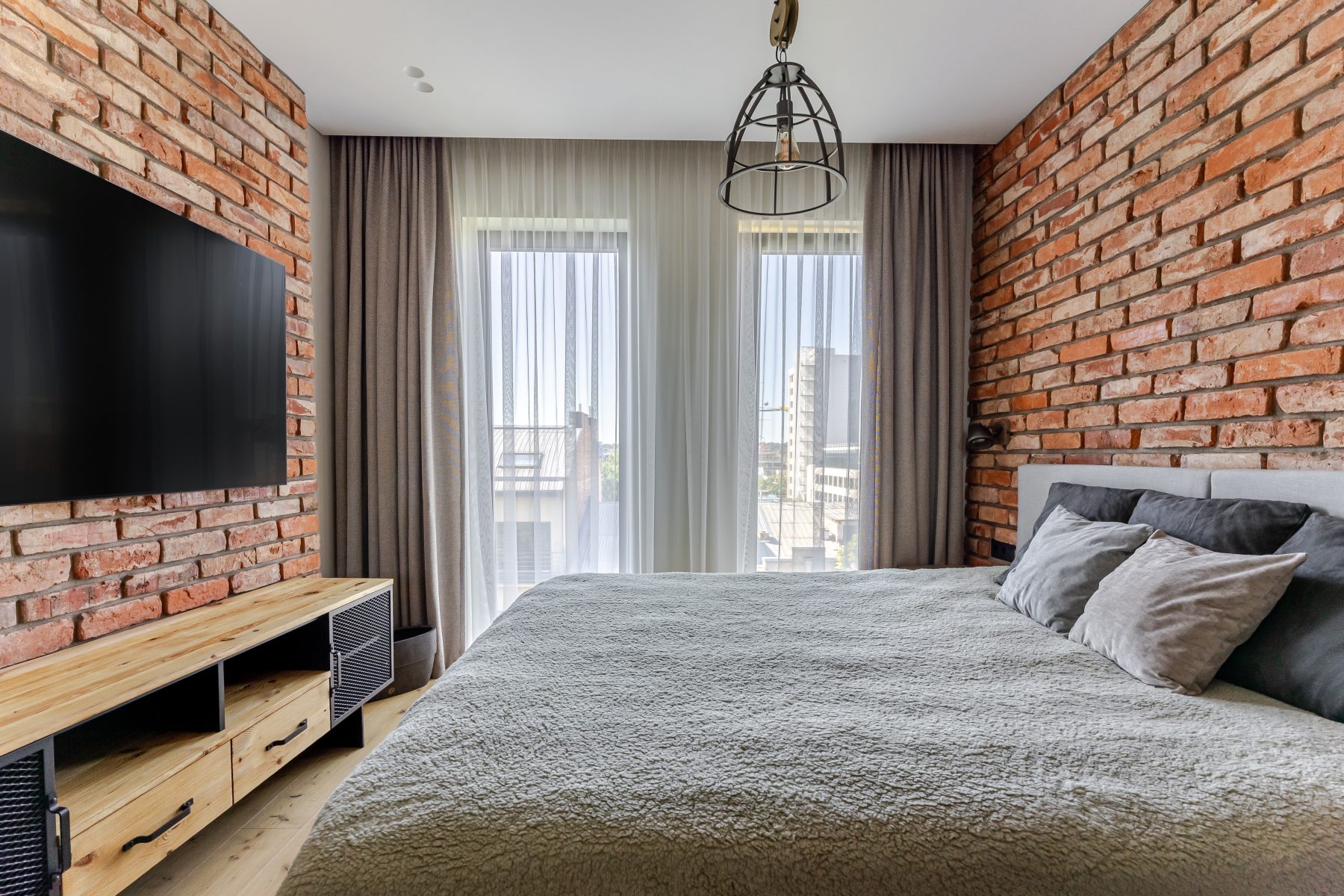 Miegamasis su natūralių plytų siena ir dideliais langais